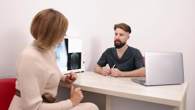 Doctor Consultation, Health Consultation, Treatment Plan. During medical consultation, doctor and patient examine X-ray images on lightbox, while referencing data on laptop.