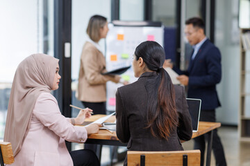 Business Asian people, laptop and conversation with research, teamwork and connection in the office. Group, employees and accounting with computer, internet and cooperation with meeting and planning