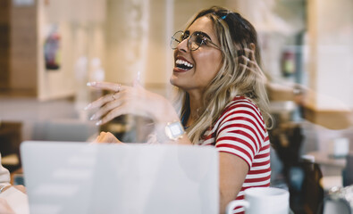 Smiling millennial hipster girl students having conversation about online courses using modern laptop computer, cheerful young women share ideas and communicating on meeting in cafeteria