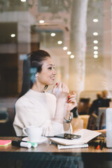Beautiful positive female colleagues having conversation about remote work in cafeteria using laptop computer, smiling hipster girl students sitting near window in cafe together communicating