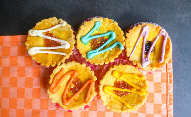 Set of variety mini pies with colorful toppings on a white plate. small tart cakes and pies on gray background with orange napkin, top view