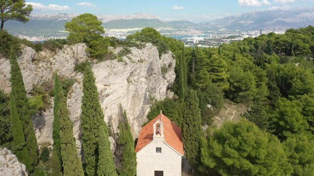 Aerial footage of the historic St. Jerome's Church (Sveti Jere) perched on Marjan Hill in Split, Croatia, surrounded by dense Mediterranean greenery and bathed in sunlight.