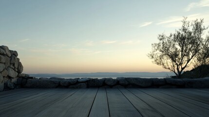 Serene sunset view from wooden deck with stone wall and tree.