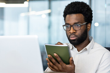 Business meeting online conference, man close up with notepad writing down data and studying remotely sitting inside office with laptop, businessman watching webinar online broadcast.