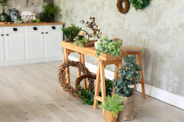 Wooden table on which there are green plants in flowerpots, watering can, flowers on a background of a grey wall. Living room in rustic style in summer. Flowers shop. Interior workplace florist.	
