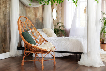 Interior boho design bedroom with garland flowers and plants. Cozy light bedroom in Scandinavian style bedroom, canopy bed and wicker rattan armchair. Bed decorated flowing white curtains canopies.   © stock_studio