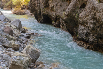 Steep cliffs hang over mountain river with emerald-clear water. Stormy Chegem River flows in deep crevice along bottom of Chegem Gorge. In depths of gorge, semi-darkness reigns.
