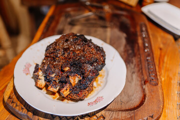 A plate of roasted beef ribs with a crispy, caramelized crust, served on a rustic wooden table, showcasing rich textures and flavors.