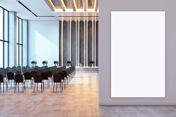 Modern conference hall interior with rows of chairs, a stage, and a blank vertical poster on the...