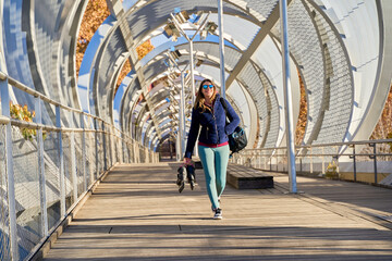 Sportswoman walking on modern bridge carrying inline skates