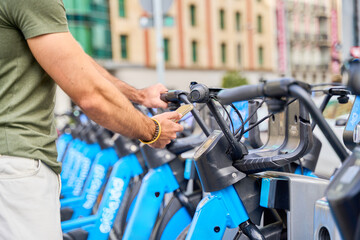 Man using smartphone at city bike-sharing station with blue bicycles