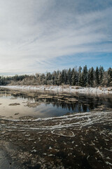 A winter landscape with a river with ice floes and a clear blue sky with snow-covered trees.