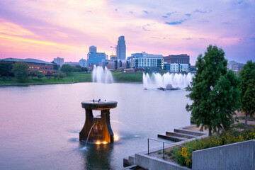 View of Omaha Nebraska skyline at sunset seen from Heartland of America Riverside Park with lake in...
