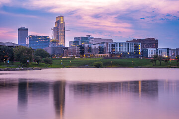 View of Omaha Nebraska skyline at sunset seen from Heartland of America Riverside Park with lake in view.