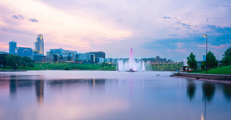 View of Omaha Nebraska skyline at sunset seen from Heartland of America Riverside Park with lake in view.