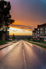 Fototapeta premium road down the mountain past apartment buildings with an impressive sunset after the rain