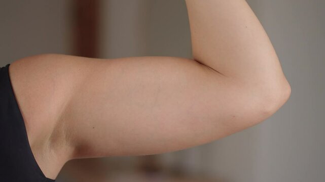 Close up of female flexing arm muscles in a home indoor. Female Biceps.
