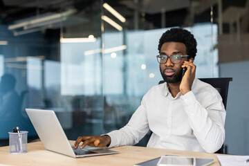 Obraz premium Portrait of serious confident businessman, man thoughtfully looking at camera, working inside office at workplace with laptop, talking on phone.