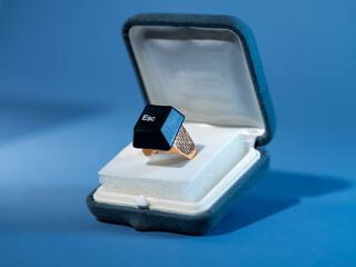 Close-up of a computer esc key on a gold ring in a ring box