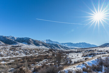 Sunny winter day in a mountain gorge, sun disk with rays and glare on the lens. Airplane trail in...