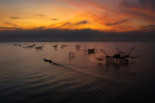 Silhouette of a boat sailing past traditional fishing nets and platforms on Pak Pra river at sunrise, Phatthalung, Thailand