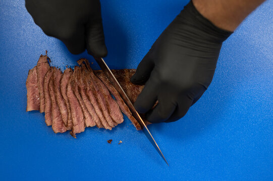 Close-up overhead view of a man slicing meat on a blue shopping board