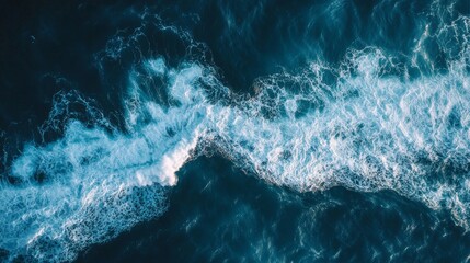 Fototapeta premium Aerial shot capturing the dynamic movement of ocean waves with white foam against a deep blue sea, showcasing nature's beauty.