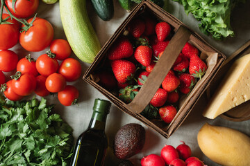 Overhead view of fresh strawberries, avocados, tomatoes, cucumbers, radishes, coriander, olive oil and cheese on a table