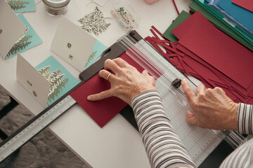 Overhead view of a woman sitting at a table making homemade Christmas cards