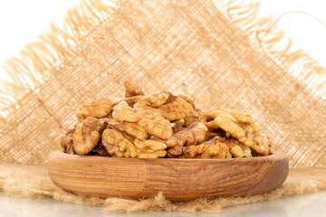 Shelled walnuts on a wooden plate with a jute napkin, close-up, isolated on a white background.