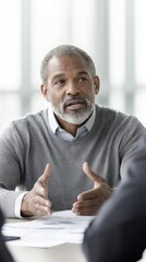 A professional man engaged in a discussion, gesturing while sitting at a table with others, showcasing leadership and communication skills.