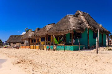 A beach with a row of colorful houses with thatched roofs
