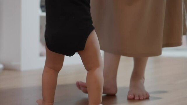 Close up toddler's feet as take their first steps, A baby padding across the warm wooden floor guided by the loving presence of a mother, Movement and determination of the child