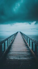 Fototapeta premium A tranquil pier extends into a mysterious blue fog, creating a serene atmosphere. The wooden walkway invites solitude and exploration over calm waters.