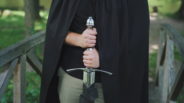 Steel sword in hands of medieval, ancient knight, monk. Close-up. Monk in cloak and with a sword, rapier in hands. Warrior ready for battle, repel an attack, defend monastery from attack by Crusaders.