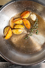 Golden-brown roasted potatoes in a skillet, sizzling in oil. Fresh thyme and garlic add flavor. A vibrant, appetizing scene ideal for culinary themes and recipes.