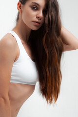 Fototapeta premium Young caucasian female with long brown hair in white tank top posing confidently