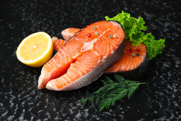 Fresh raw salmon steaks with spices, lemon, lettuce and dill on dark textured table, closeup