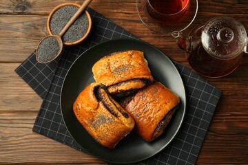 Tasty buns with poppy seeds served with tea on wooden table, flat lay