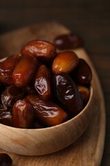 Tasty sweet dried dates in bowl on wooden board, closeup