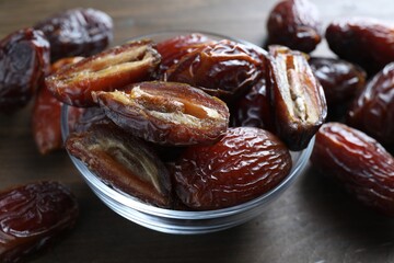 Many tasty dried dates in bowl on wooden table, closeup