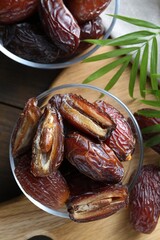 Many tasty dried dates in bowls and leaves on table, top view