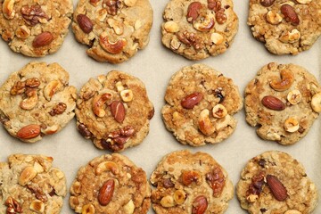 Tasty cookies with nuts on parchment paper, top view