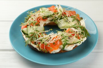 Half of delicious bagel with salmon, microgreens, arugula and cream cheese on white wooden table, closeup