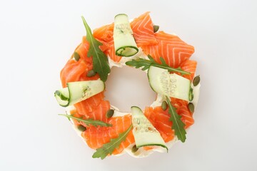 Half of delicious bagel with salmon, cream cheese and cucumber on white background, top view