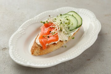 Delicious bruschetta with salmon, cream cheese and cucumber on light table, closeup