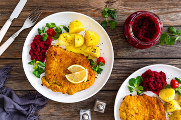 Breaded fried pork chop with boiled potatoes, fresh vegetables and beets on wooden table	