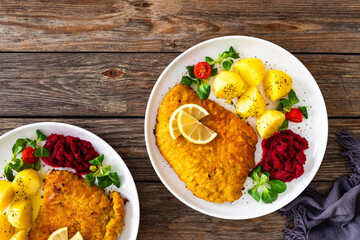 Breaded fried pork chop with boiled potatoes, fresh vegetables and beets on wooden table	