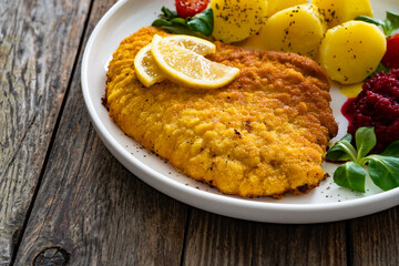 Breaded fried pork chop with boiled potatoes, fresh vegetables and beets on wooden table	