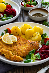 Breaded fried pork chop with boiled potatoes, fresh vegetables and beets on wooden table	